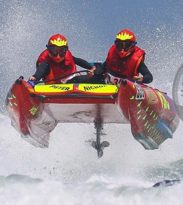 Peter and his co-pilot airborne in a red inflatable racing boat, spray flying