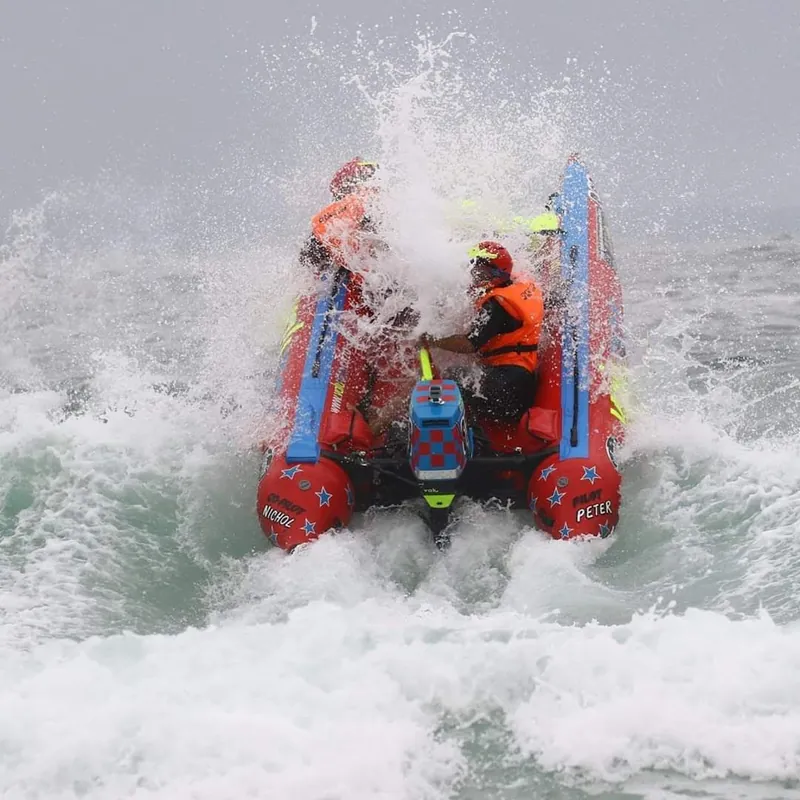 Red inflatable racing boat ploughing into a breaking wave